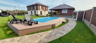 Бассейн с композитной террасой, шезлонги и дорожка из тротуарной плитки на заднем фоне жилой дом и баня
